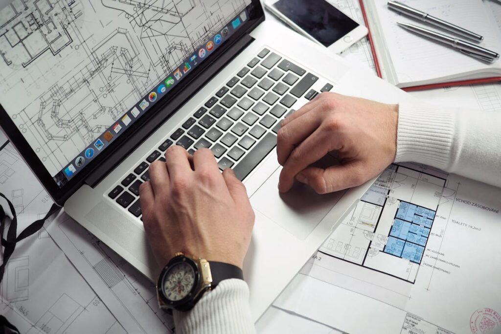 An individual with 25 years of experience, working on a laptop placed beside architectural plans and drawings for premier home builder projects in awe-inspiring communities.